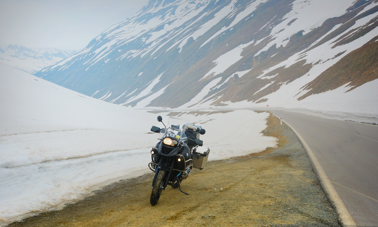 A parked motorbike on the side of a snowy and mountainous road