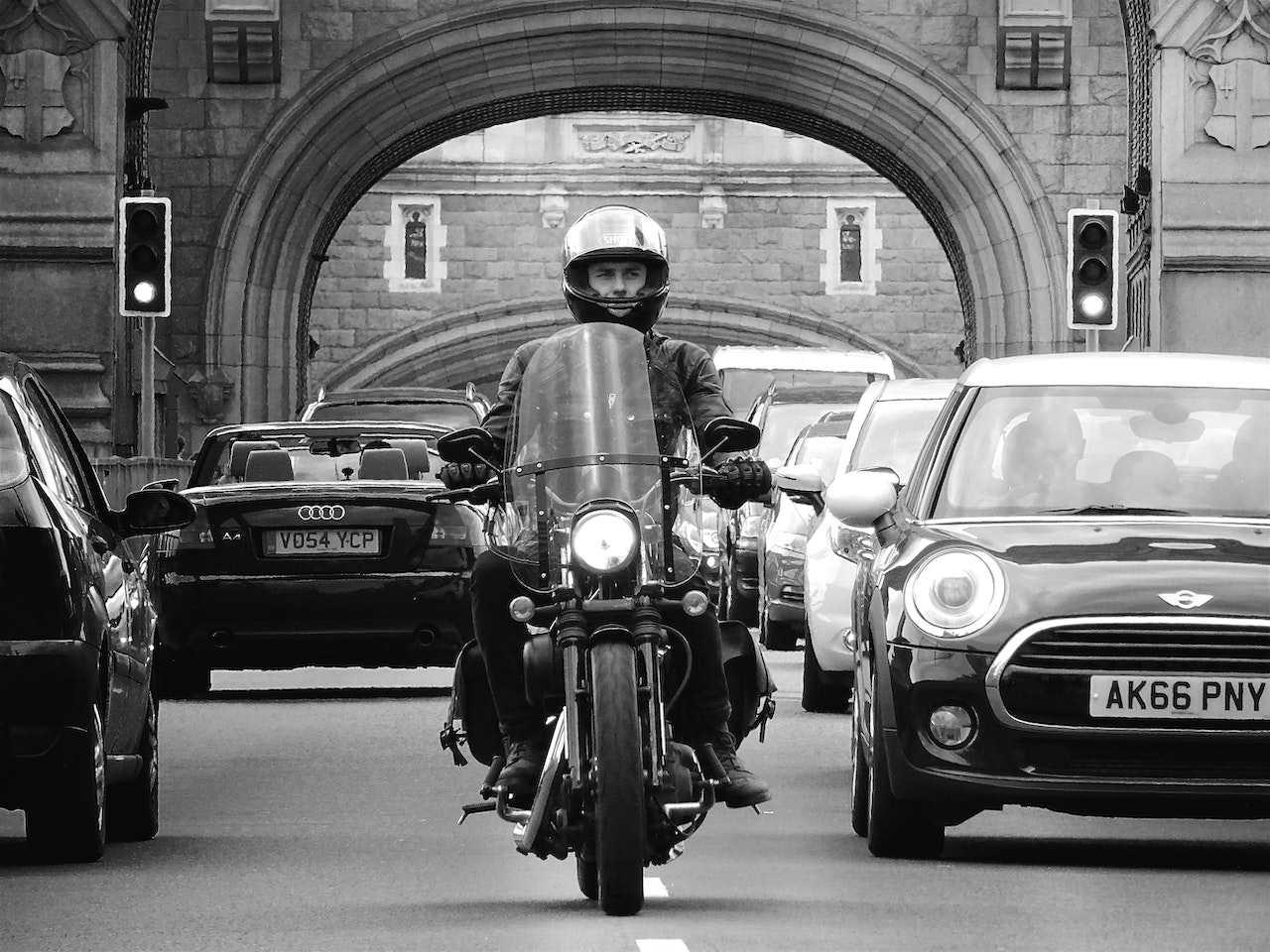 Black and white photo of a man riding a motorbike in between a row of cars