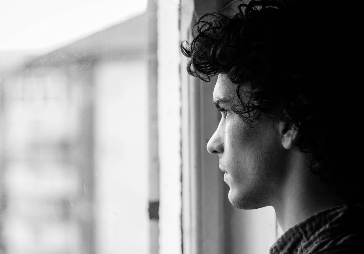 black and white image of a young man looking out of a window