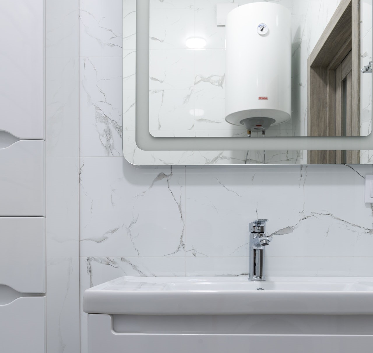 A white marble bathroom with a white boiler in the reflection of the mirror