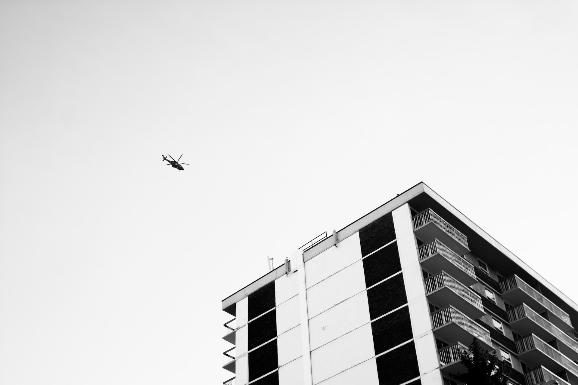 black and white image of a high rise block of flats with a helicopter in the distance