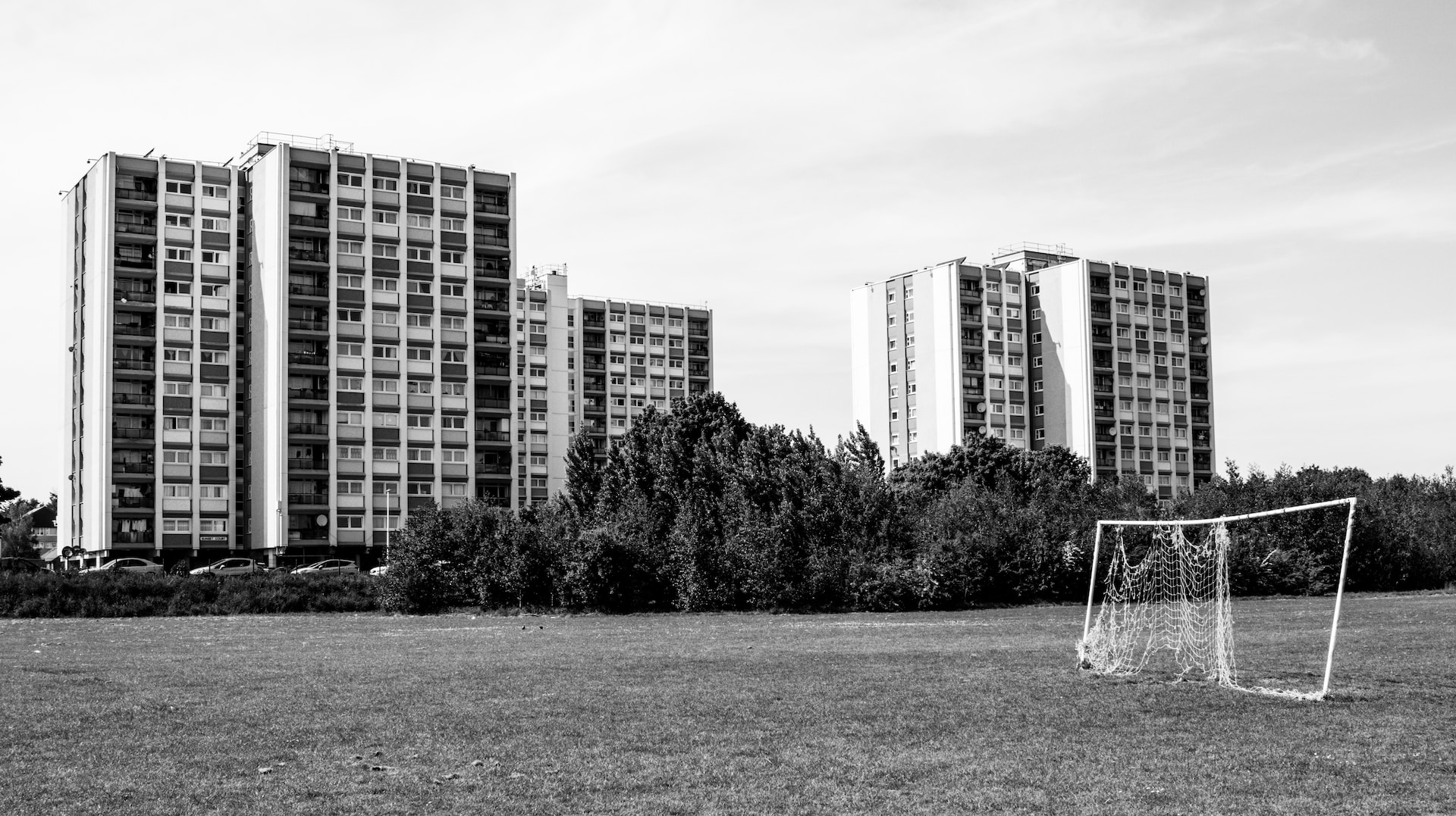 black and white photo of two blocks of high rise flats behind a football net.