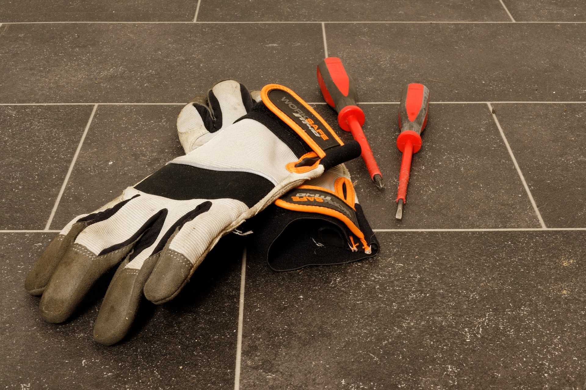 safety gloves next to two screwdrivers resting on the ground