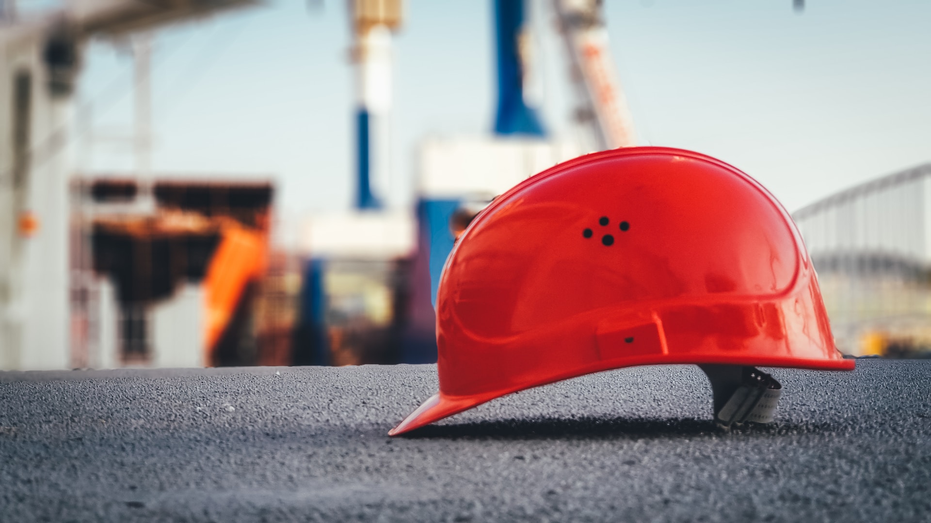 A red hard hat placed on the ground with a construction site in the background