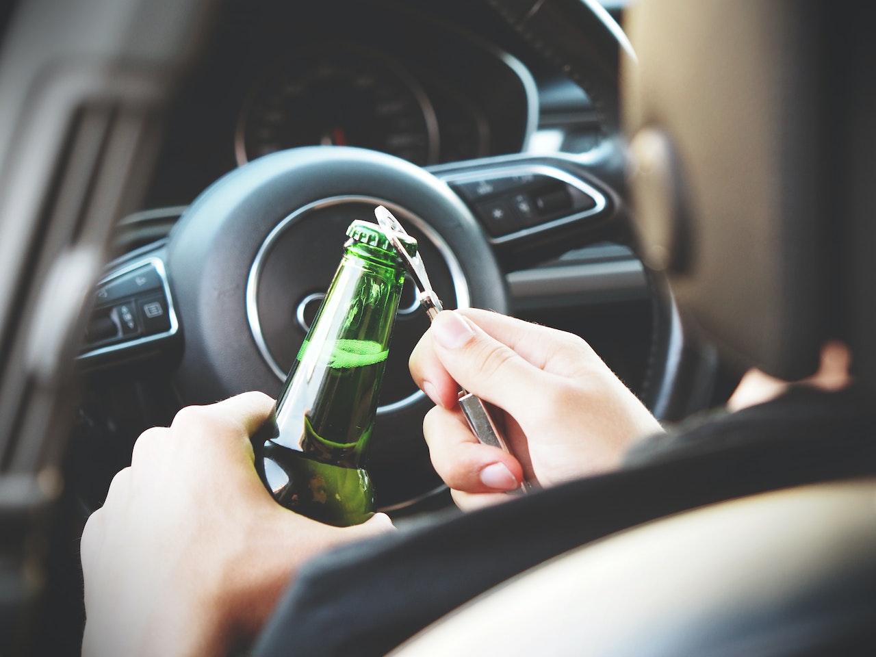 Person opening a bottle of beer behind the wheel of a car