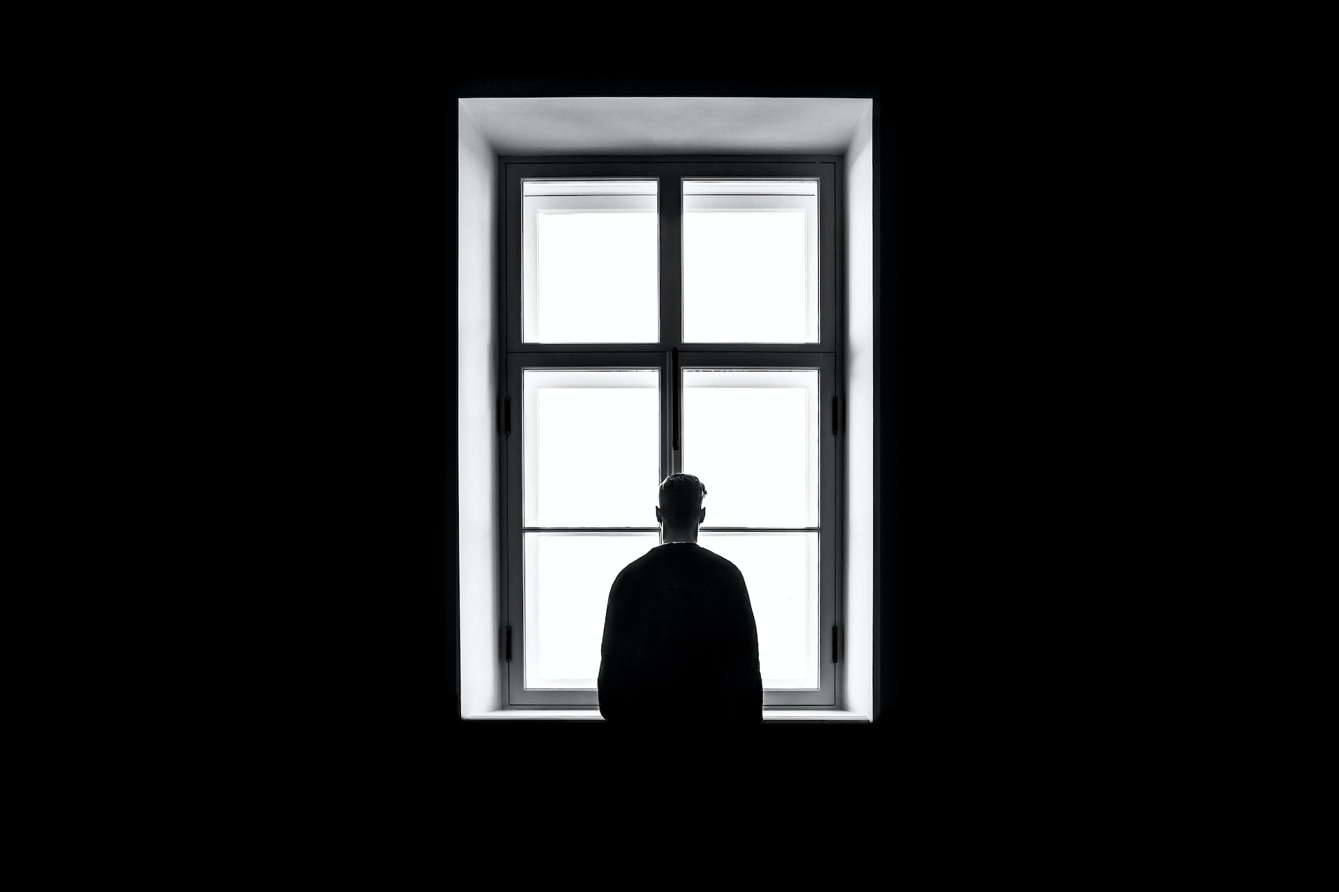 black and white photo of someone stood by a window alone