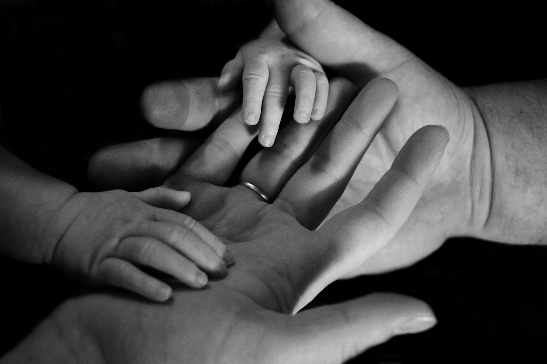 black and white photo of parents hands with their babies hand