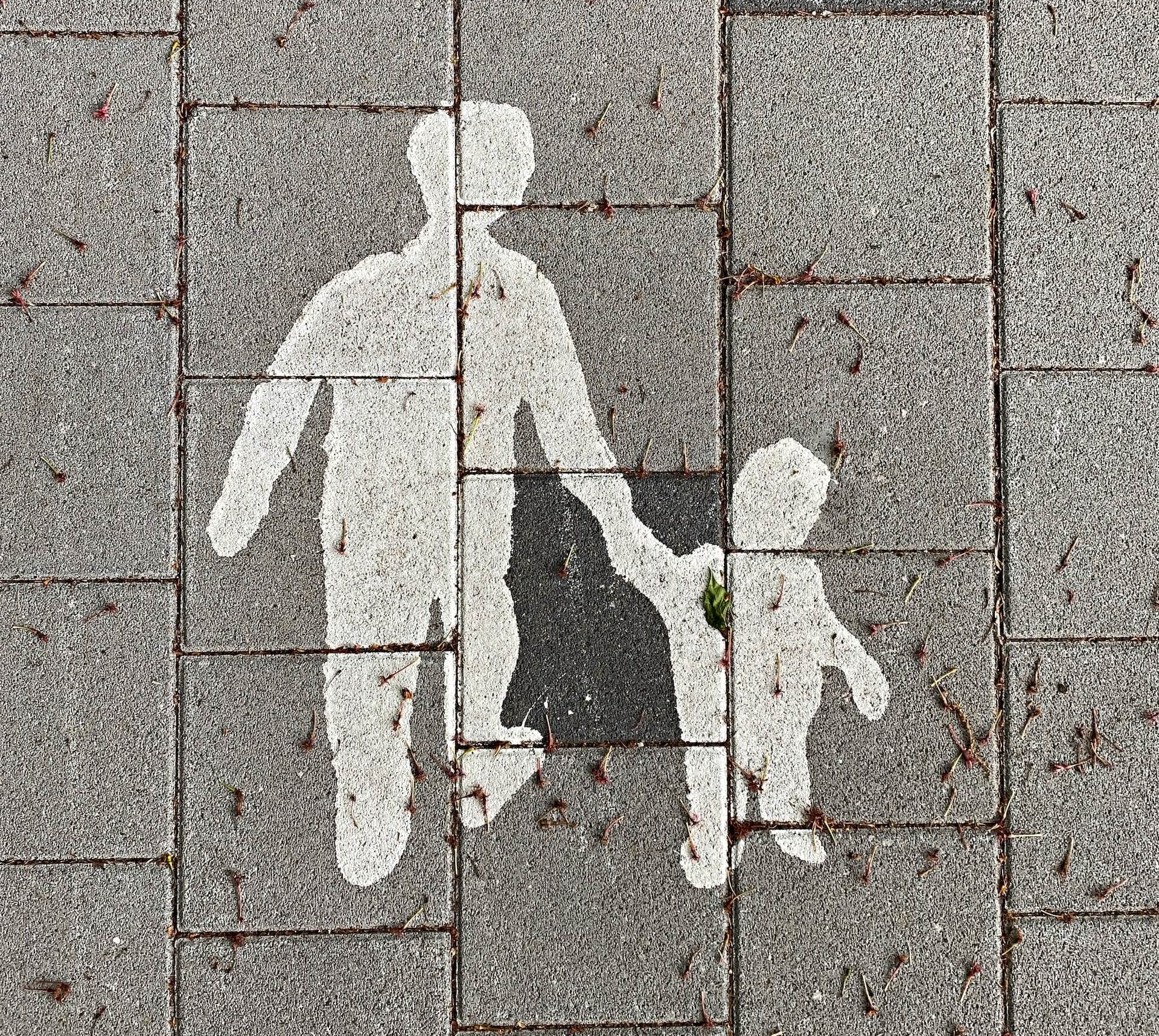 A sign on a path of a parent and child crossing the road